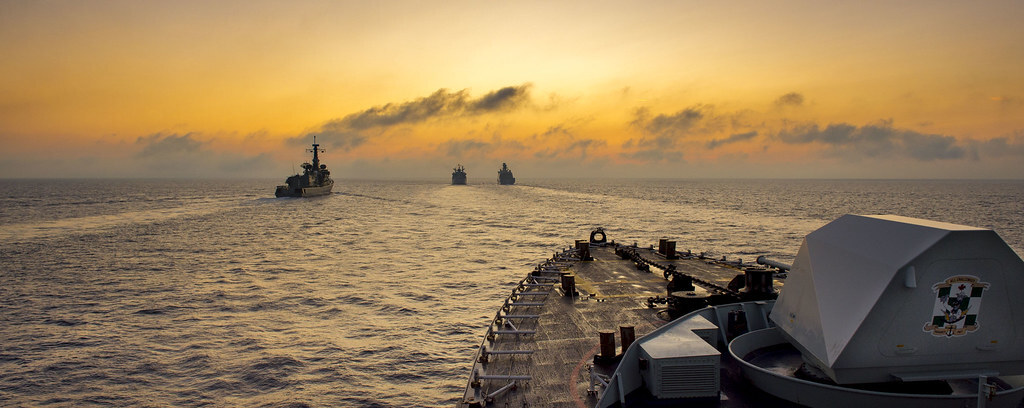 Royal Canadian Navy ships sailing in formation at sunset, seen from the bow of a warship.