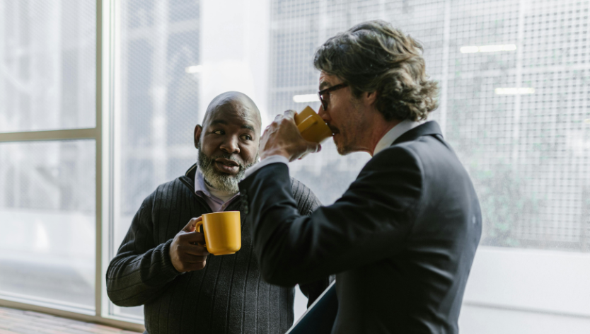 Two men talking while drinking coffee from yellow mugs.